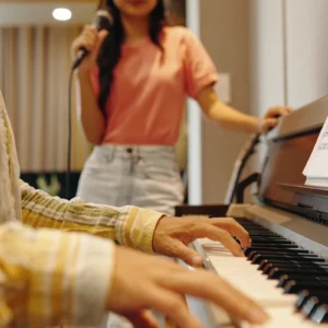 Person playing piano, another singing nearby.