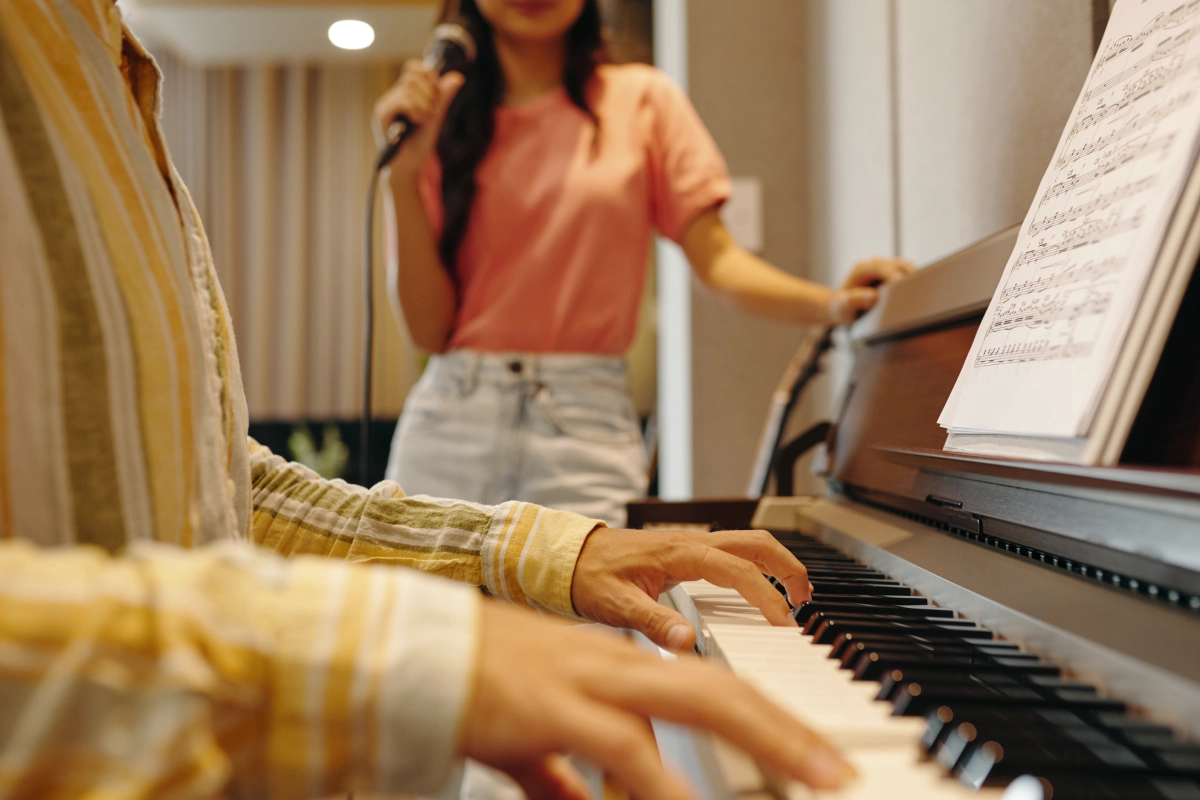 Person playing piano, another singing nearby.