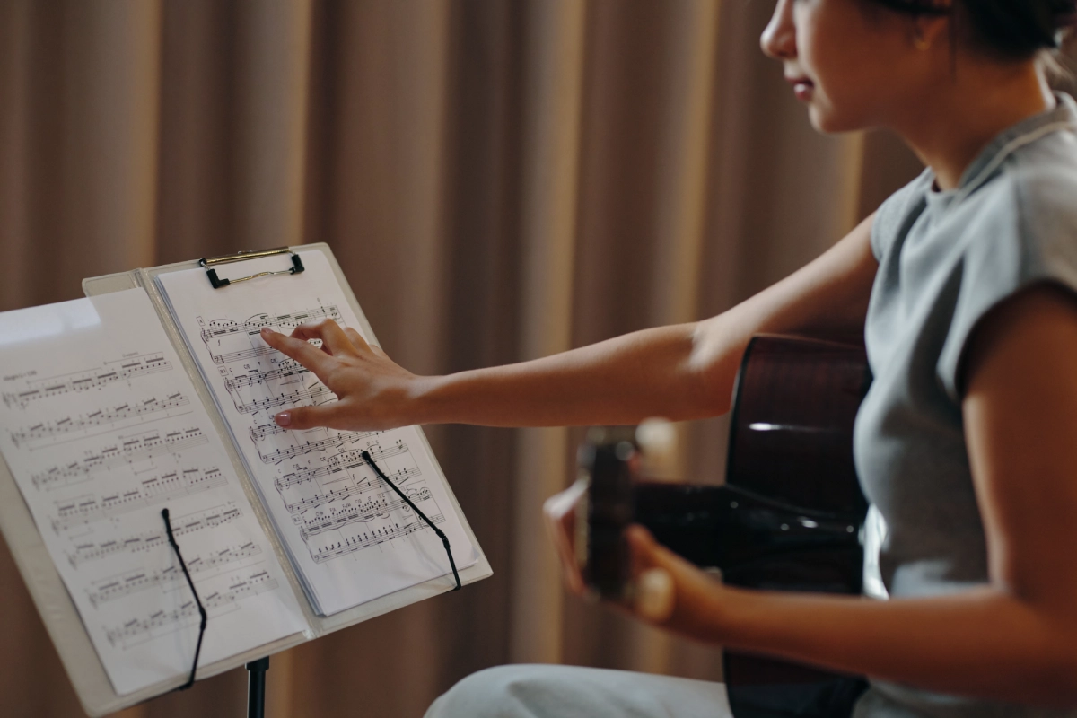 Person playing guitar, reading sheet music.