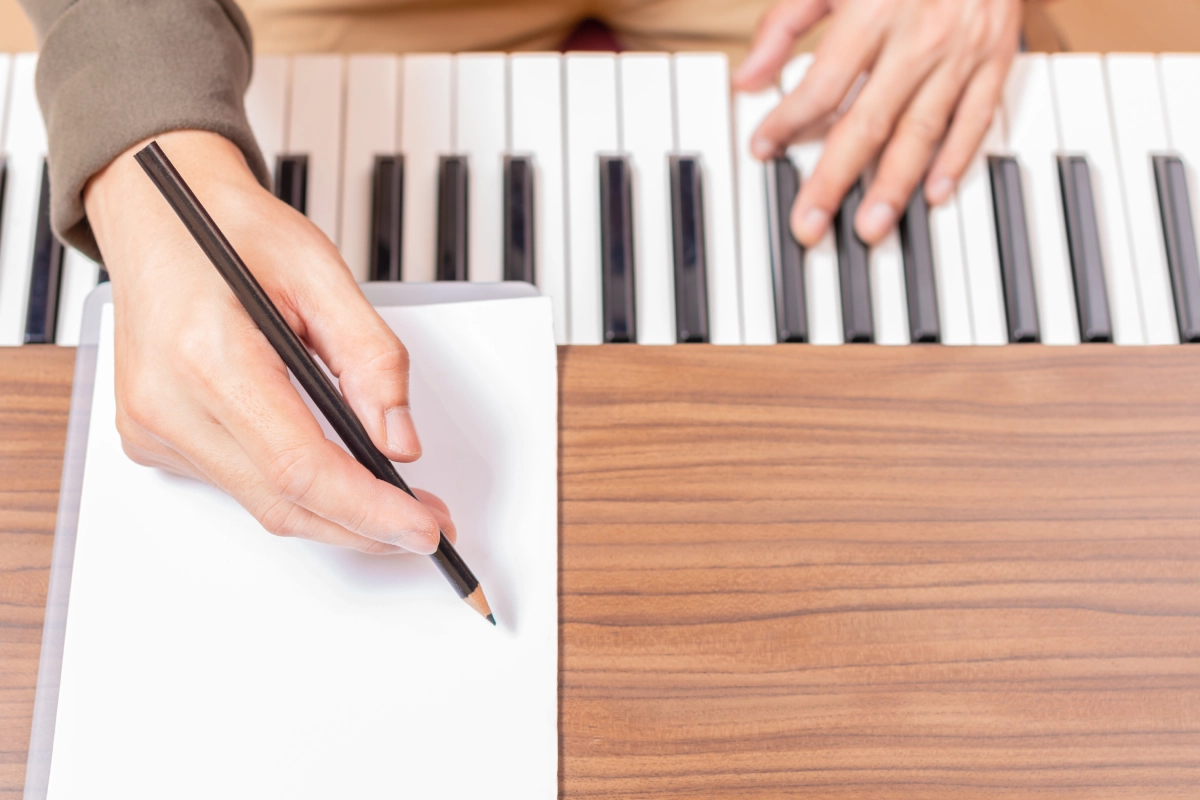 Hands writing and playing piano keyboard.