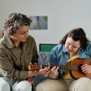 Two people playing ukulele on a sofa.