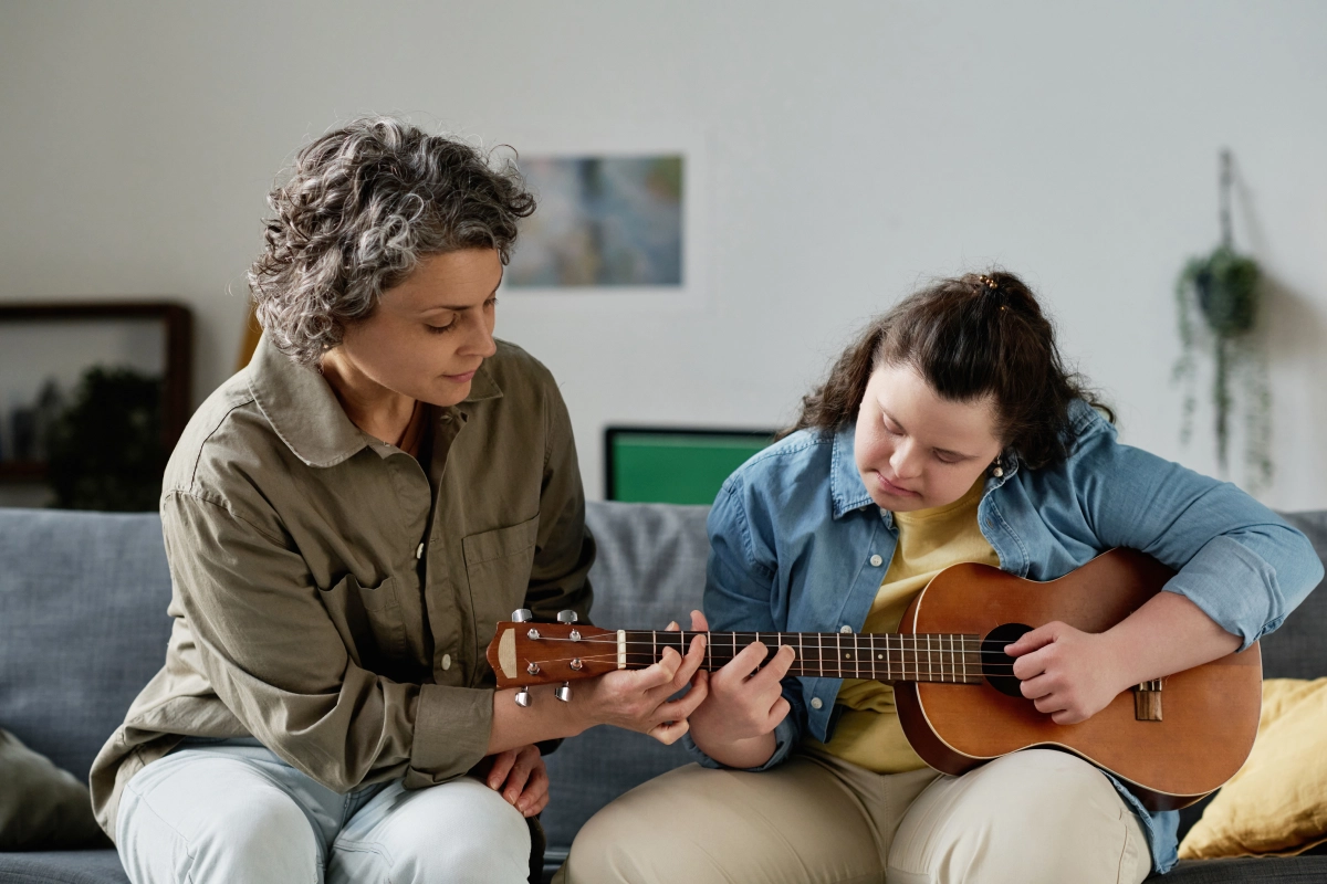 Two people playing ukulele on a sofa.
