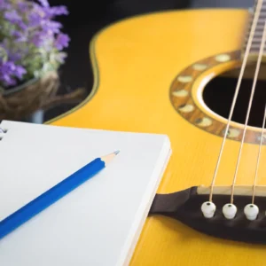 Guitar, notebook, pencil, and purple flowers.