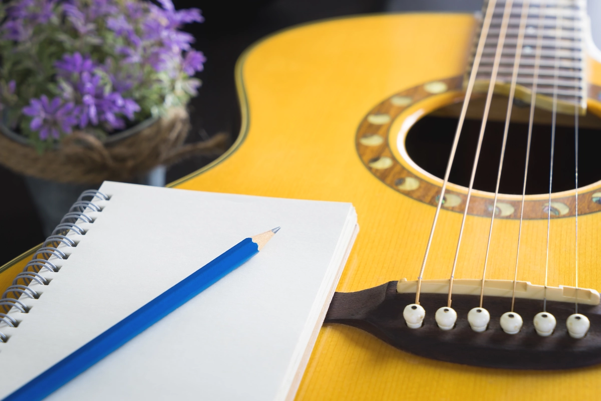 Guitar, notebook, pencil, and purple flowers.