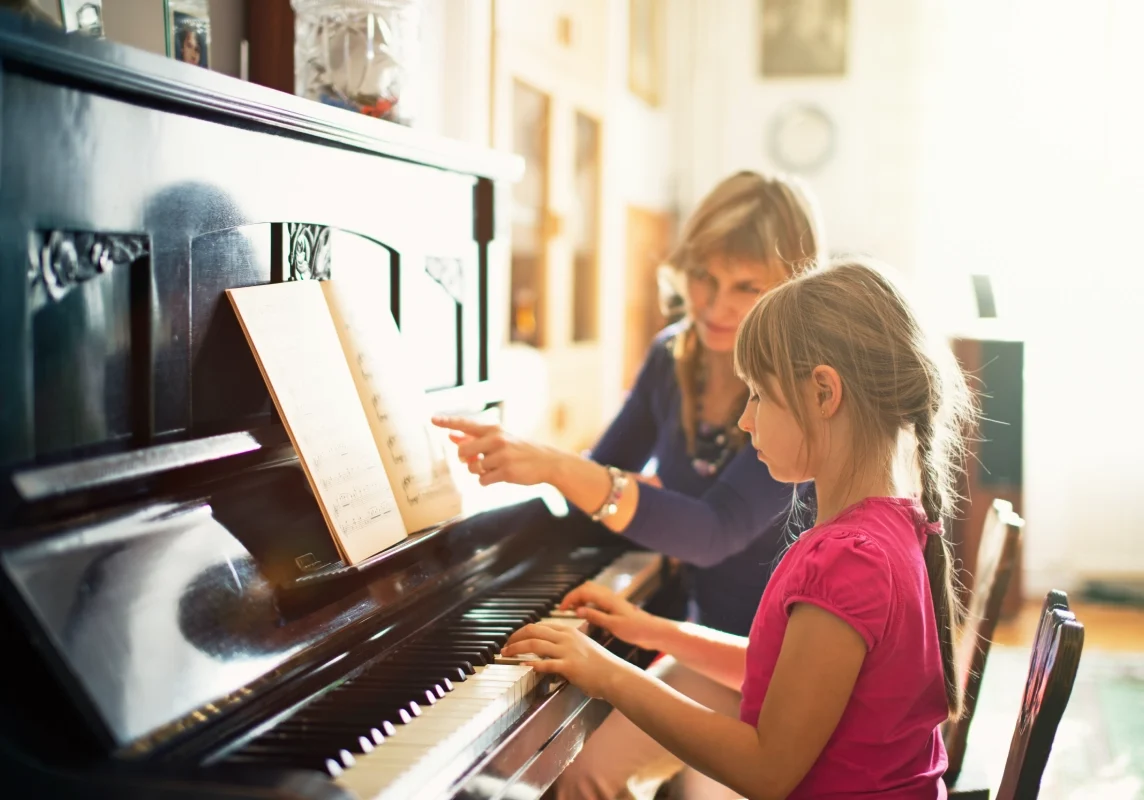 Child learning piano with adult guidance.