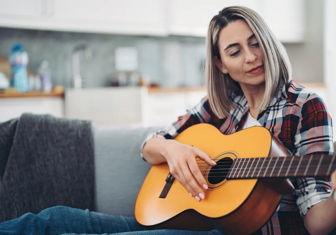 Woman playing acoustic guitar on a couch.