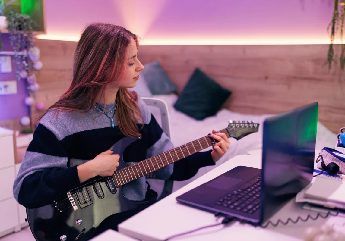 Woman playing electric guitar near laptop.