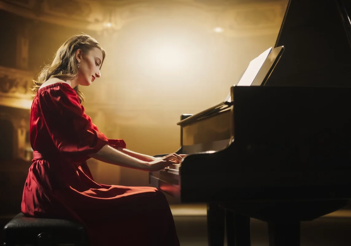 Woman in red dress playing piano onstage.